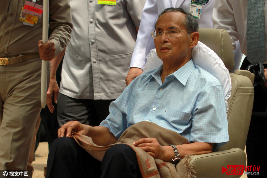 图为2009年10月23日，泰国国王普密蓬-阿杜德出现在曼谷诗里叻医院接受治疗。当天普密蓬国王身穿蓝色短袖衬衫和黑色裤子，坐在一辆轮椅上，在诗里叻医院一层向已故母亲和泰国曼谷王朝五世王朱拉隆功的塑像敬献花环。23日恰逢泰国公共假日——五世王纪念日，不少泰国民众前往诗里叻医院为普密蓬国王签名祈愿。当国王出现时，等候在那里的民众不禁流下热泪，高呼“陛下万岁”。