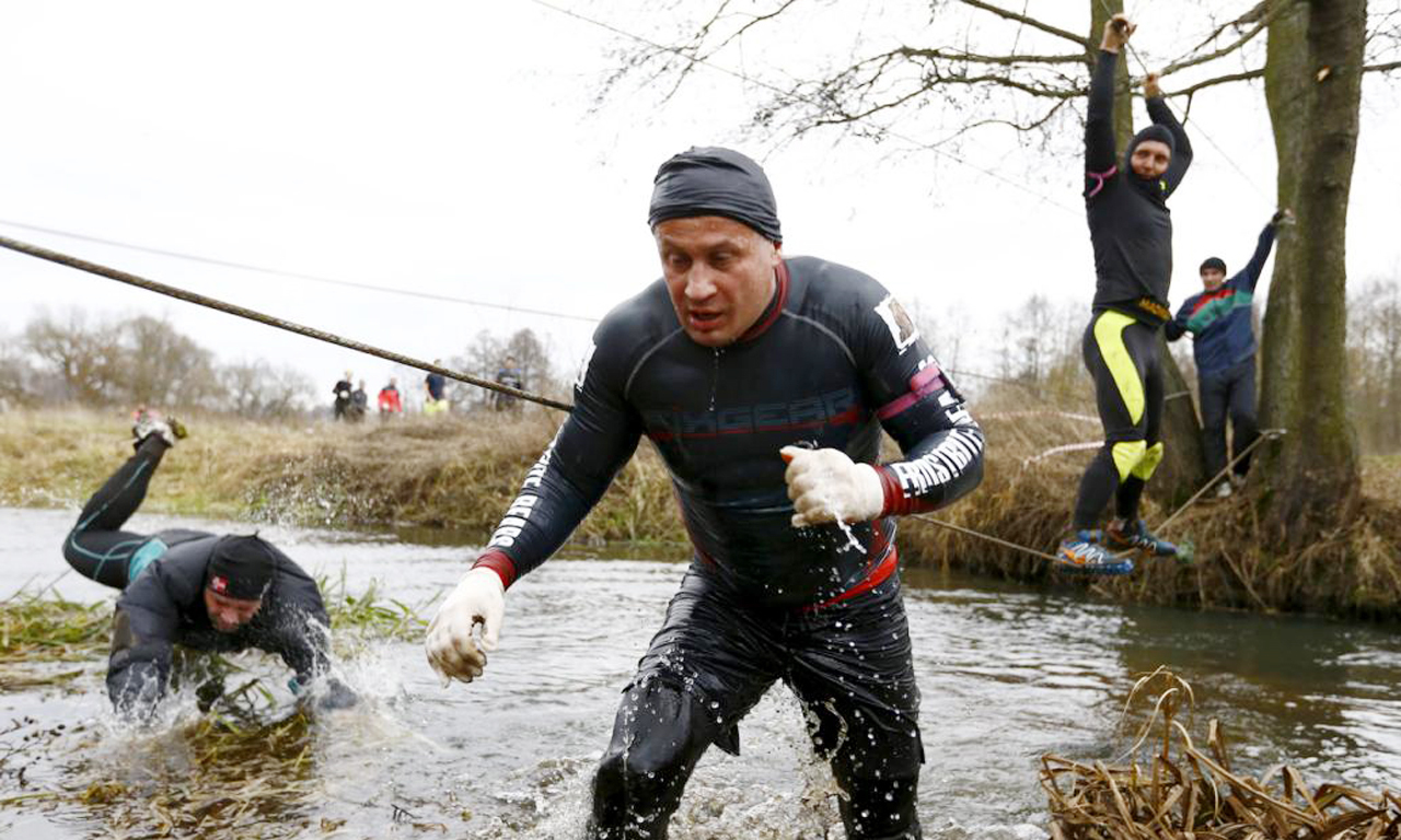 比赛过程中，会有很多泥坑、爬绳、黑暗的隧道、铁丝网和其他考验勇气和痛苦的障碍。图为选手爬铁丝穿过河流。
