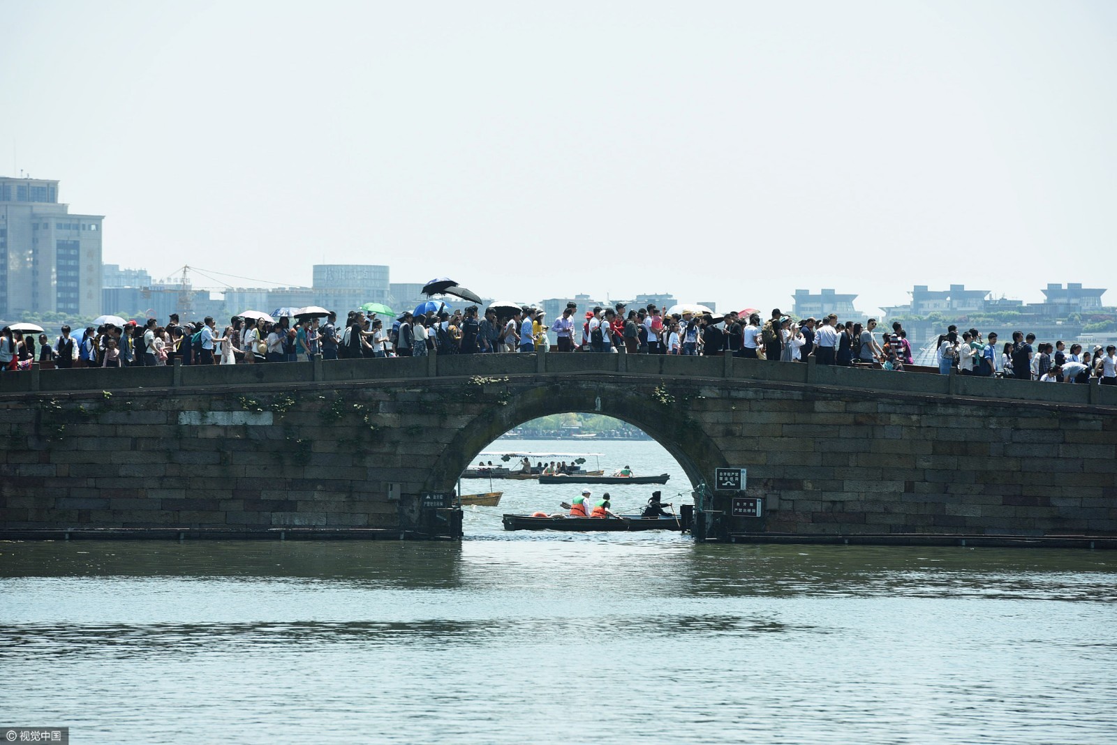 一艘手划船从杭州西湖边密集的游客边上驶过.图片来源:视觉中国