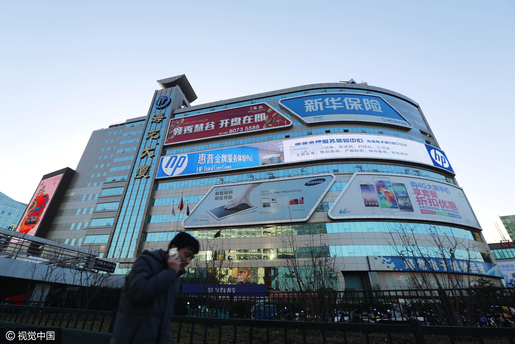 2015年01月31日，北京，一位市民从贴满广告牌的海龙大厦前走过。在中国IT的启蒙时代，以海龙为代表的一批电子卖场强势崛起，成为让电子产品经销商日进斗金的黄金商圈。但近些年传统电子卖场逐渐萎缩，风光不在。