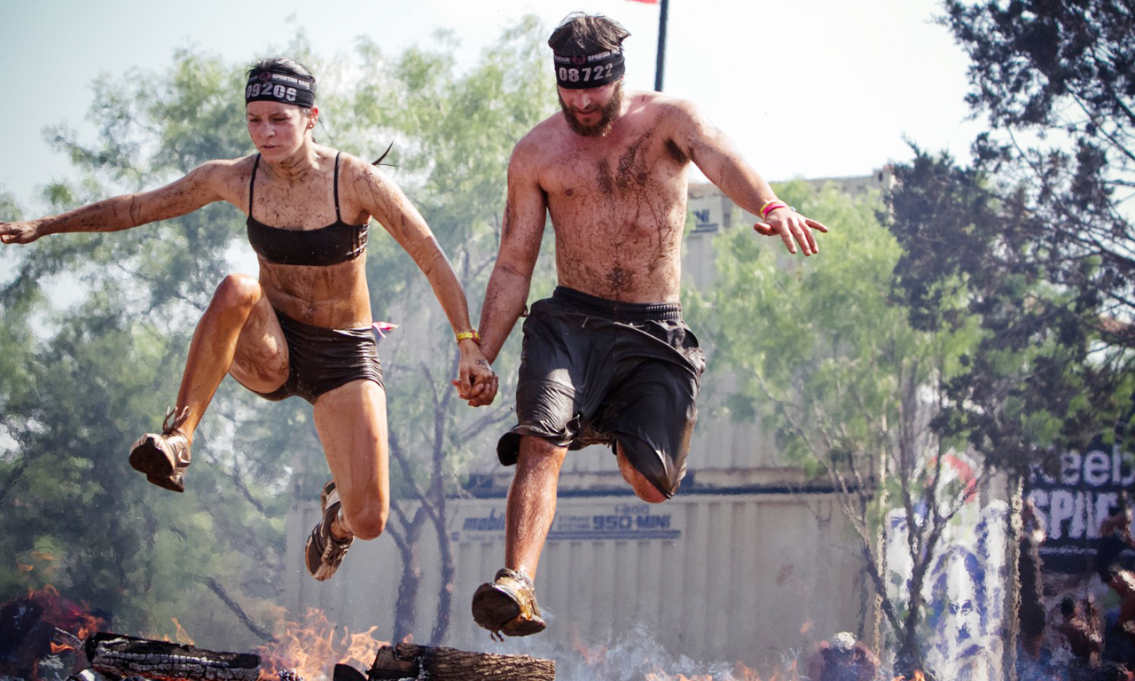 这项系列赛主要的内容包括：设有15个障碍的3英里冲刺；超级斯巴达，设有20个障碍的8英里穿越；斯巴达野兽，设有25个障碍的12英里穿越；最后是死亡竞赛，每年举行一次的48小时耐力赛。图为一对情侣拉手跳过火堆。