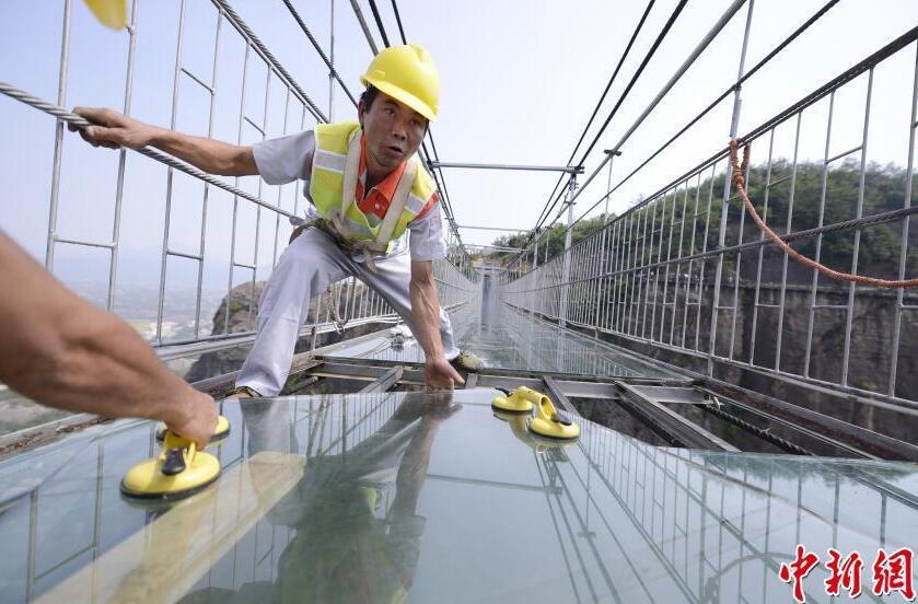 维修工人系着安全绳在高空进行更换玻璃的工作。