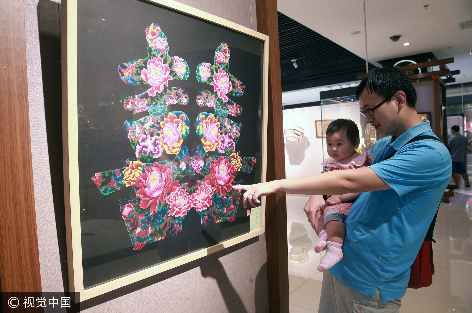 2017年9月3日，一位家长抱着孩子在北京工艺美术创新设计大赛作品展上观赏美术作品《喜从天降》。