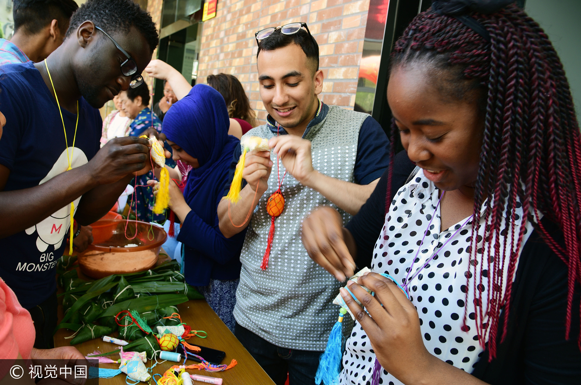 2017年5月25日,江苏镇江,社区居民在指导外国留学生包粽子。当日,端午节临近,江苏大学十多名来自赞比亚、印度、土耳其、巴基斯坦、南非等国的留学生走进镇江市和平路街道金江社区,在居民指导下学习包粽子、缝香囊,在咸鸭蛋上描画端午民俗,体验中国传统的端午文化。