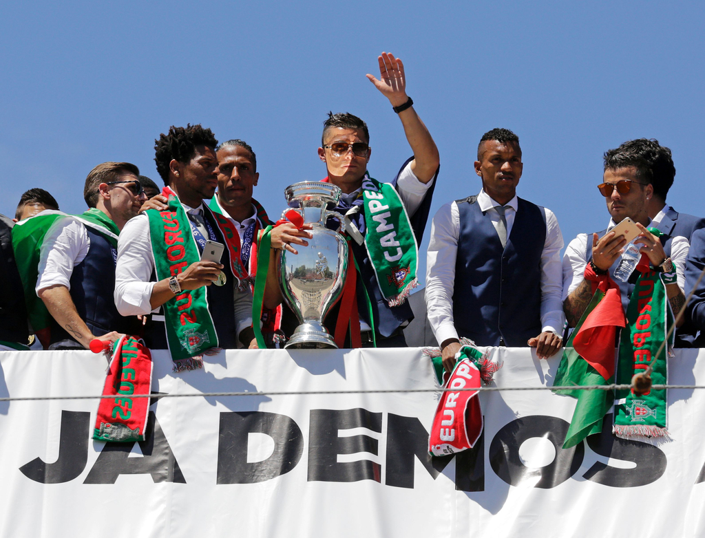 2016年7月11日，葡萄牙里斯本，2016年欧洲杯冠军葡萄牙队回到国内，全体队员和教练乘坐大巴游行并受到葡萄牙总统的接见，全城民众欢欣舞动狂欢庆祝。图为C罗与队友向球迷致意